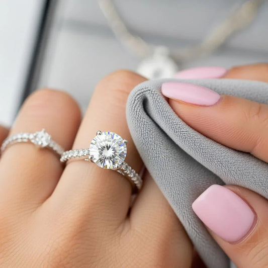 Hand with pink nails cleaning diamond engagement ring and wedding band with gray cloth
