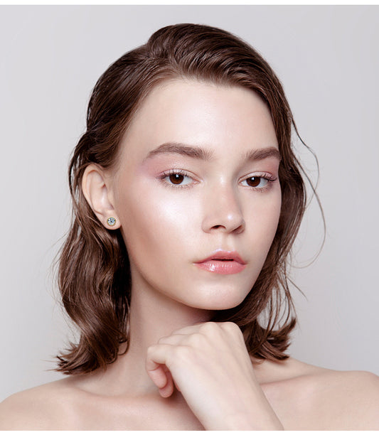 Woman wearing simple round stud earrings with clear gemstones, natural makeup, neutral background