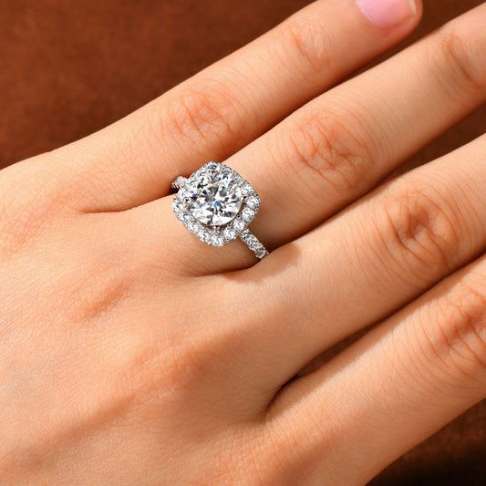 Cushion halo diamond engagement ring on hand against brown background