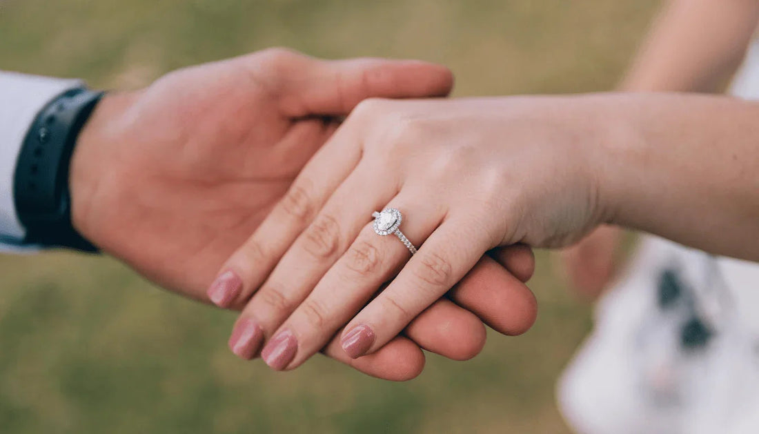 Close-up of diamond engagement ring on hand, couple holding hands outdoors