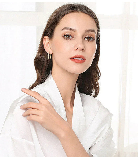 Woman in white robe wearing gold hoop earrings, natural makeup, and soft waves hairstyle